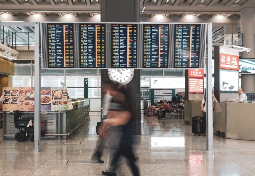 Blurred motion of travelers in a modern airport terminal with departure screens and a prominent clock.