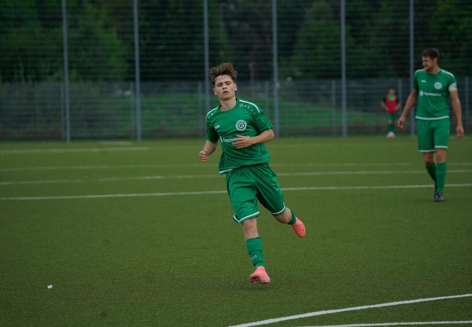 A football player in a green jersey running during an outdoor match on a grass pitch.