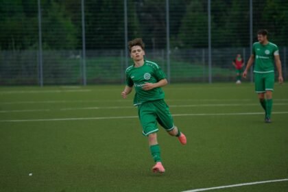 A football player in a green jersey running during an outdoor match on a grass pitch.