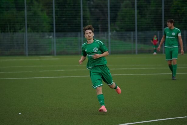 A football player in a green jersey running during an outdoor match on a grass pitch.