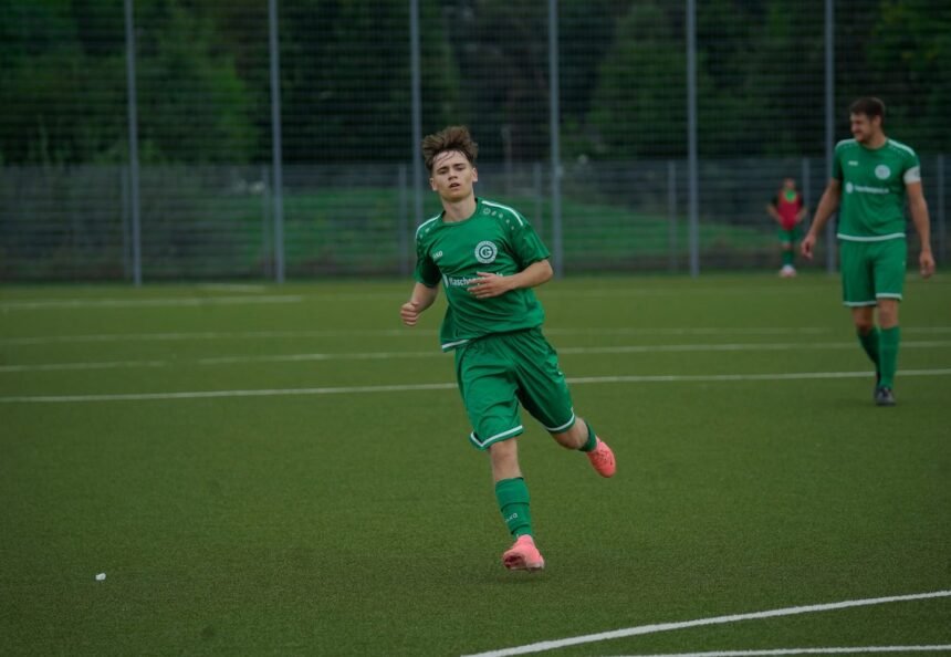 A football player in a green jersey running during an outdoor match on a grass pitch.