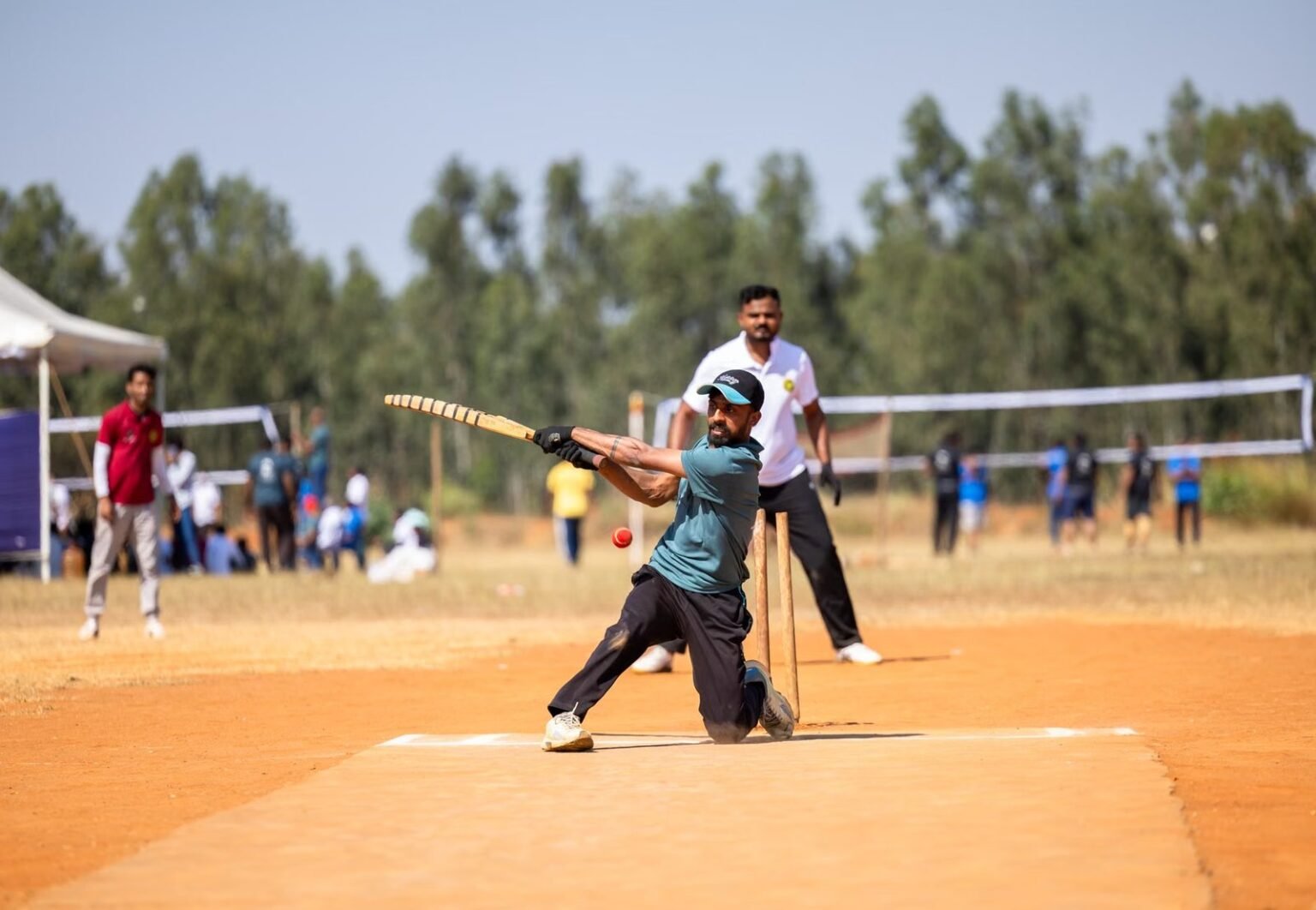 Cricket player skillfully hitting a ball during a lively outdoor match on a sunny day.