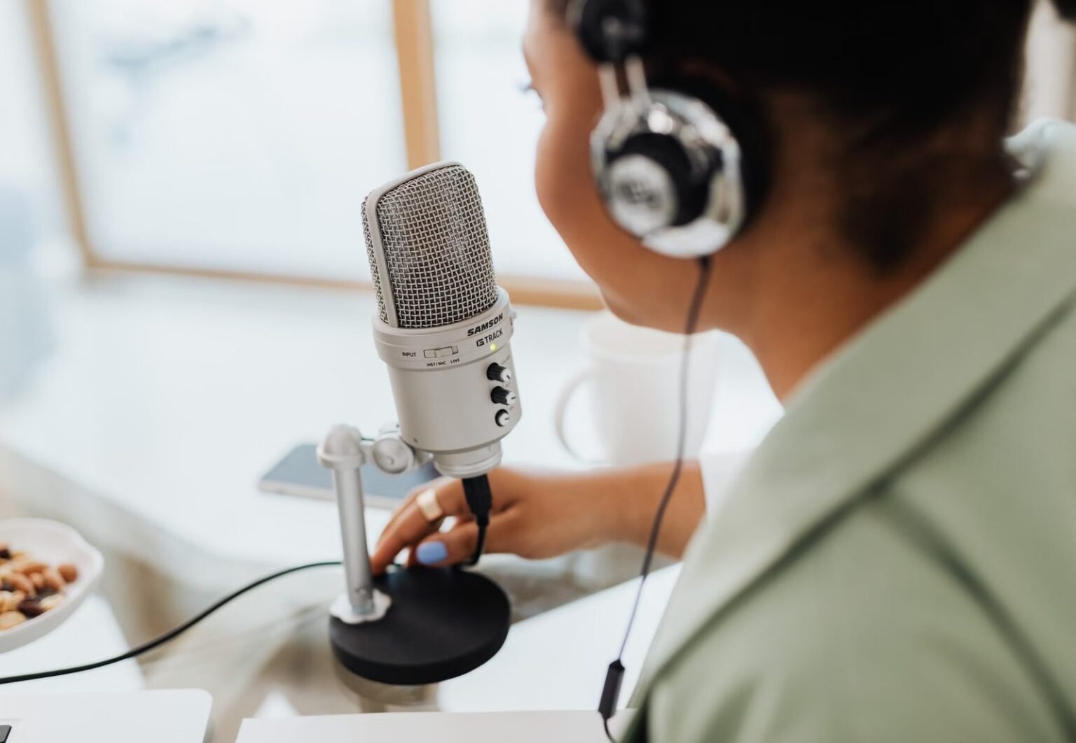 Woman using a microphone and headphones indoors, focusing on recording a podcast or voiceover.