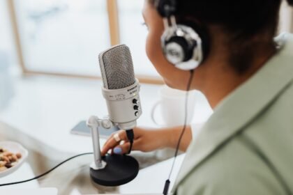 Woman using a microphone and headphones indoors, focusing on recording a podcast or voiceover.