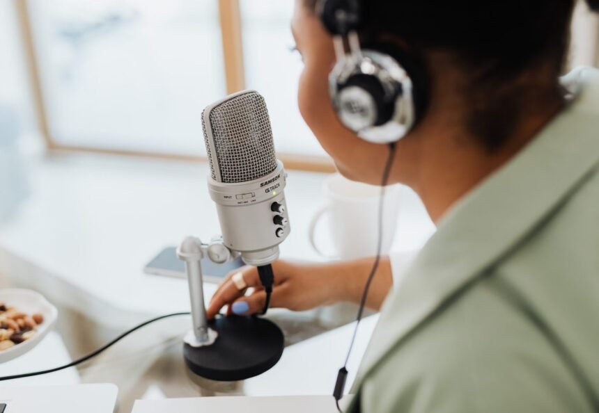 Woman using a microphone and headphones indoors, focusing on recording a podcast or voiceover.