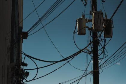Low angle view of power lines and transformers against a clear blue sky, depicting modern electricity infrastructure.