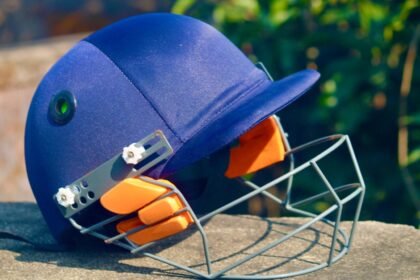 Close-up of a blue cricket helmet with faceguard placed outdoors on a sunny day.