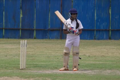 A young female cricket player poised to bat on a grassy field in Gahunje, India.