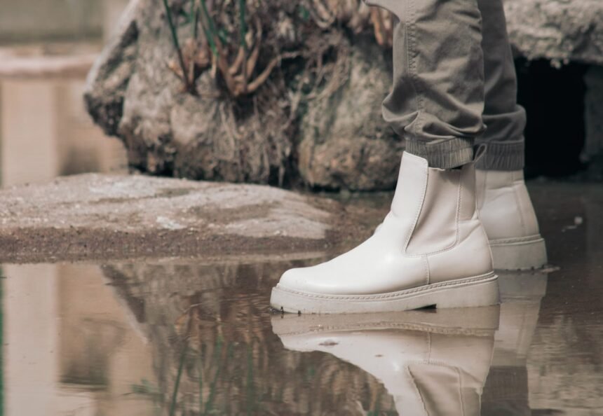 White Chelsea boots in a puddle with a rocky outdoor background, showcasing a stylish and reflective moment.