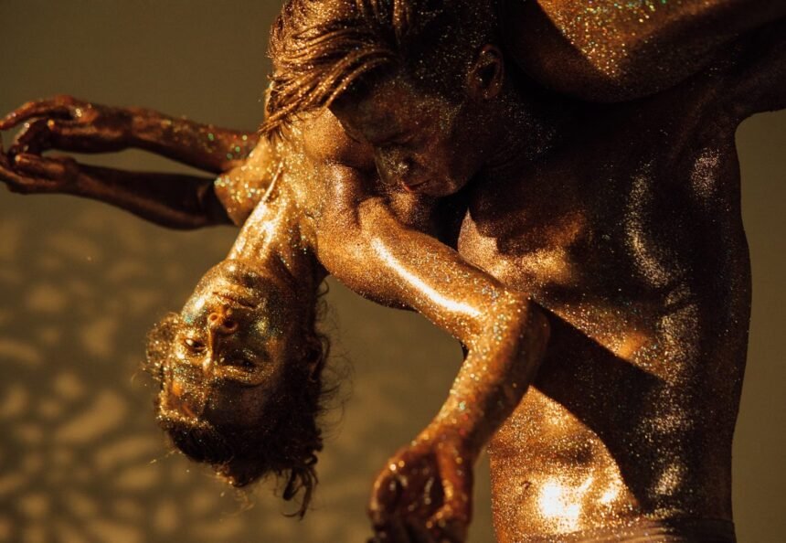 Dramatic dance performance with glitter-covered dancers in an artistic pose.