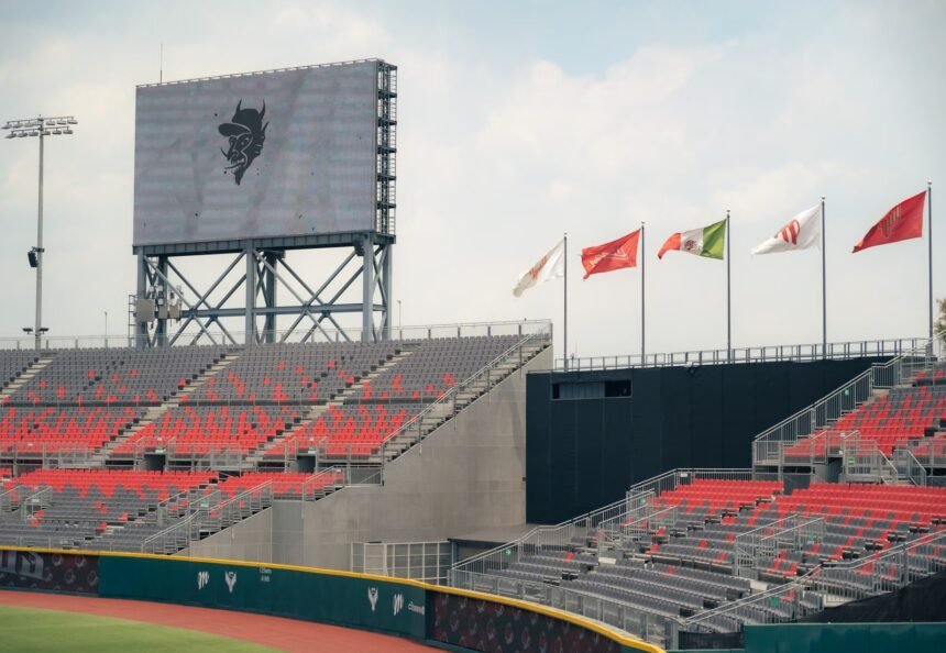 A modern stadium featuring red and gray seating and international flags, under a cloudy sky.