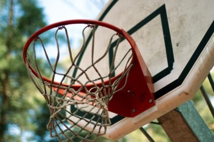 A detailed view of a basketball hoop and net against a blurred outdoor background, emphasizing a sporty feel.