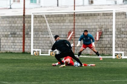 Action-packed football scene with players and a goalkeeper on green field.