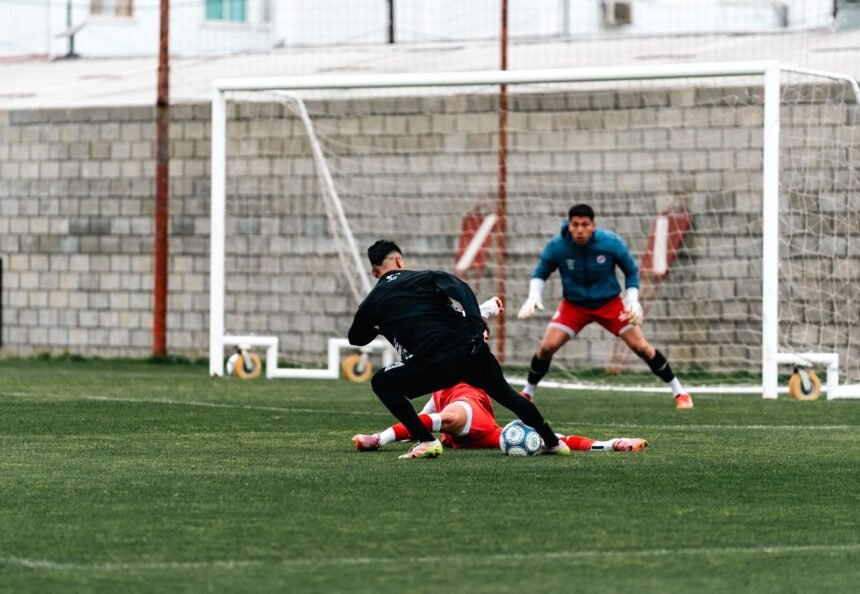 Action-packed football scene with players and a goalkeeper on green field.