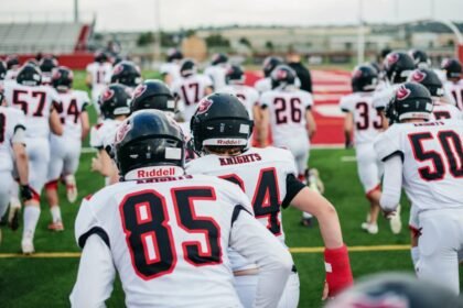 High school football team in uniforms running onto field during practice.