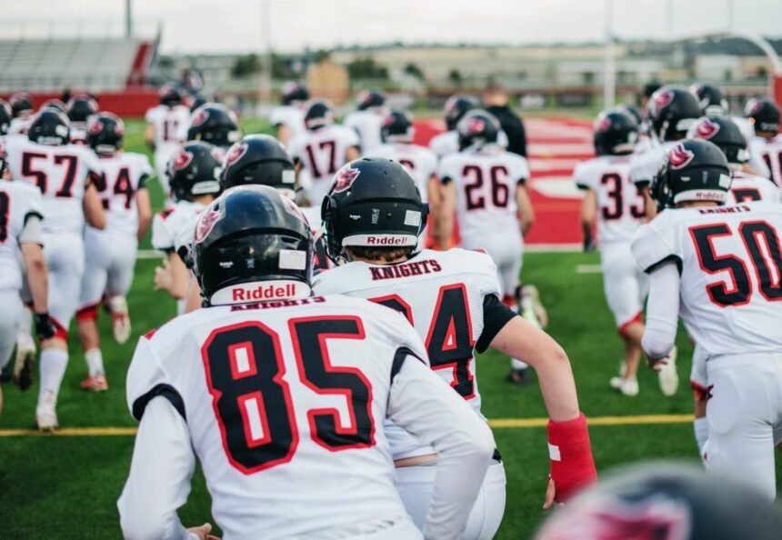 High school football team in uniforms running onto field during practice.