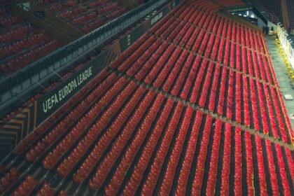 Rows of empty red seats in a UEFA Europa League stadium, captured from above.