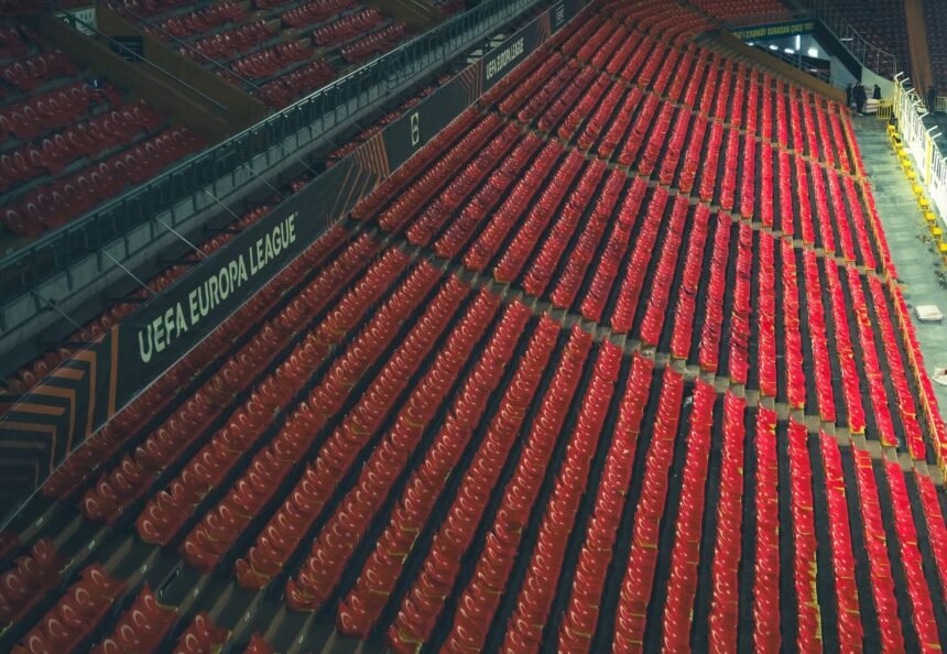 Rows of empty red seats in a UEFA Europa League stadium, captured from above.