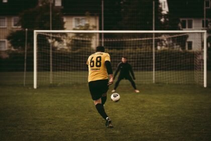 A soccer player takes a decisive penalty kick aiming to score against the goalkeeper.