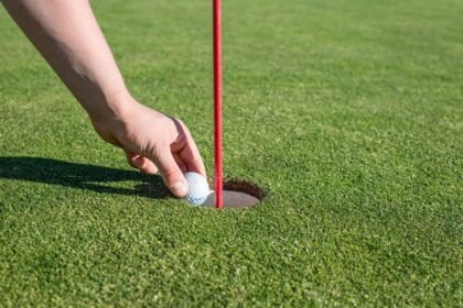 A hand retrieves a golf ball from the hole on a well-manicured green, signifying a successful putt.