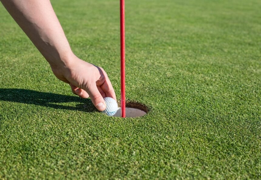 A hand retrieves a golf ball from the hole on a well-manicured green, signifying a successful putt.