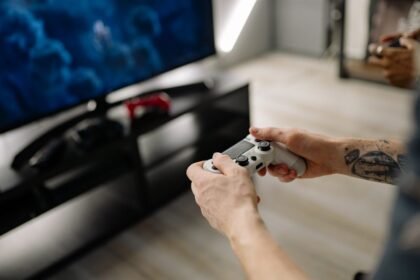 Person playing video games using a game controller indoors on a modern TV setup.