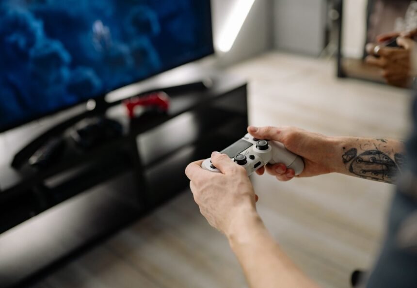 Person playing video games using a game controller indoors on a modern TV setup.