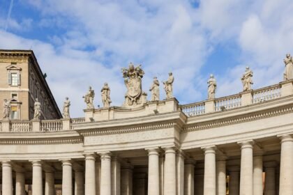 Historic colonnade and statues at St. Peter's Square under a blue sky, Vatican City.