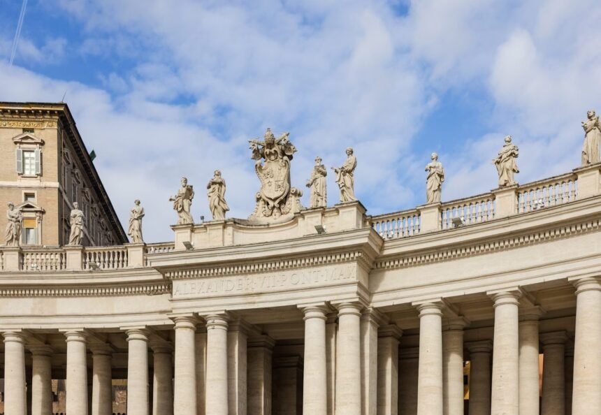 Historic colonnade and statues at St. Peter's Square under a blue sky, Vatican City.