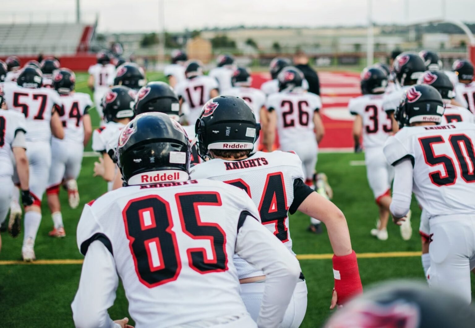 High school football team in uniforms running onto field during practice.