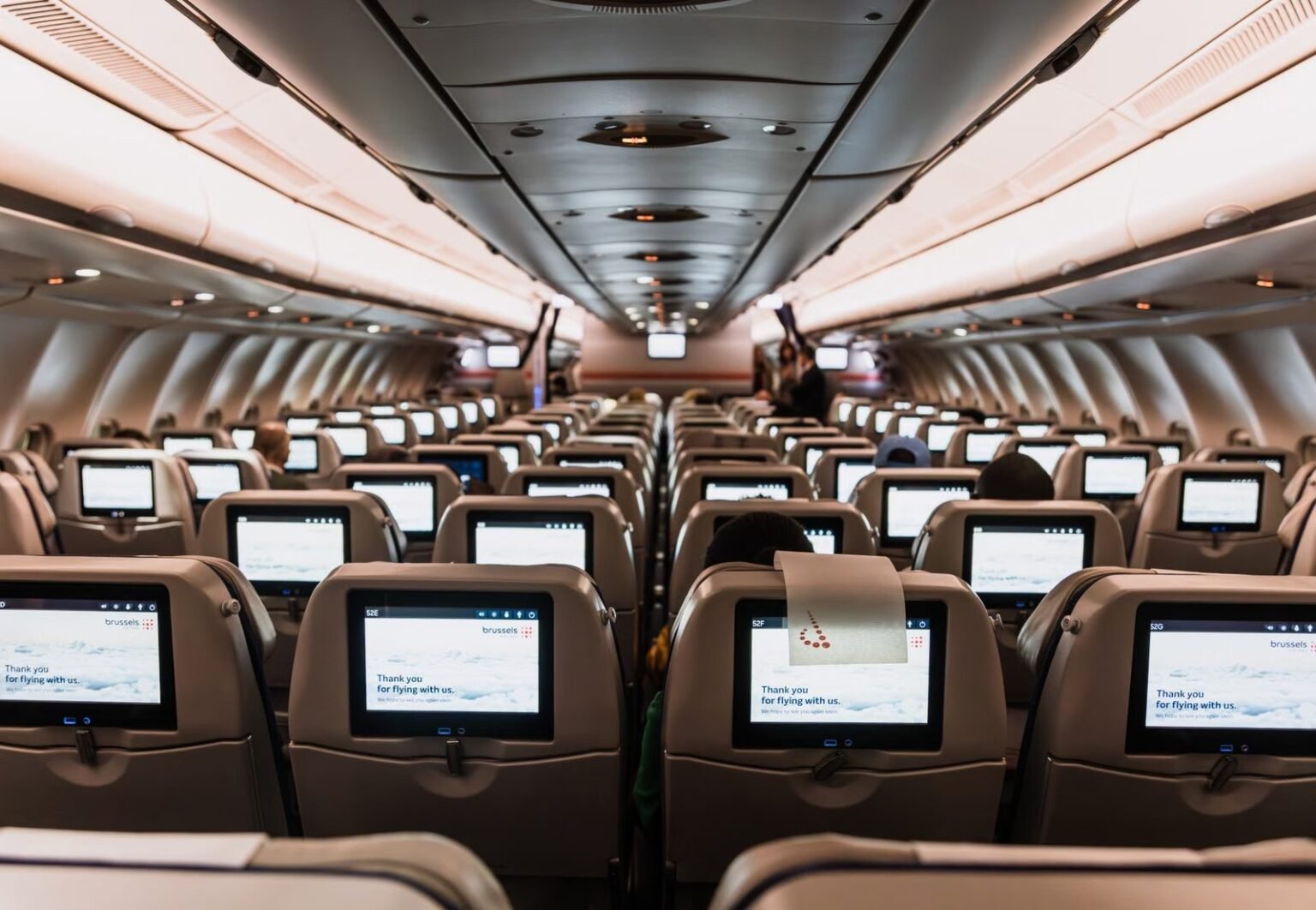 Comfortable airplane cabin interior featuring in-flight entertainment screens on all seats.