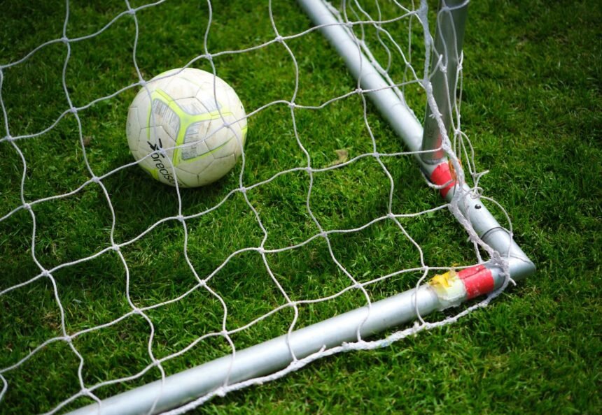 Close-up image of a soccer ball resting in a goal net on a vibrant green grass field.