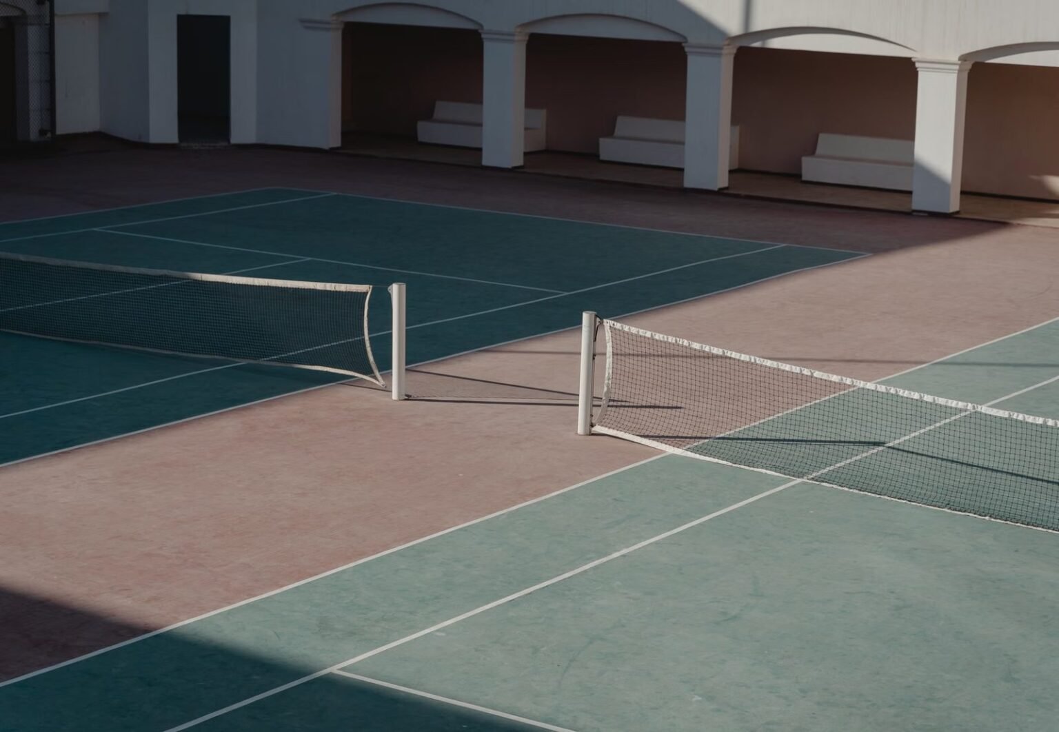 A deserted tennis court with shadows casting over the net, creating a serene atmosphere.