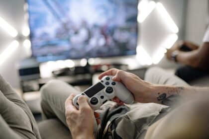 Hands holding a video game controller in a modern living room, playing on TV.