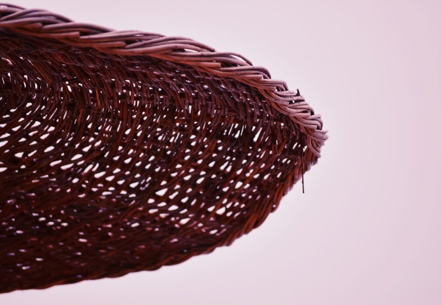 Detailed close-up of an intricately woven wicker basket against a soft pink background.