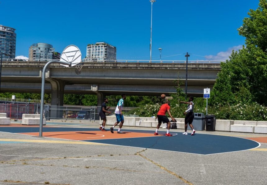 A group of friends enjoying a lively basketball game on an urban outdoor court under a clear blue sky.