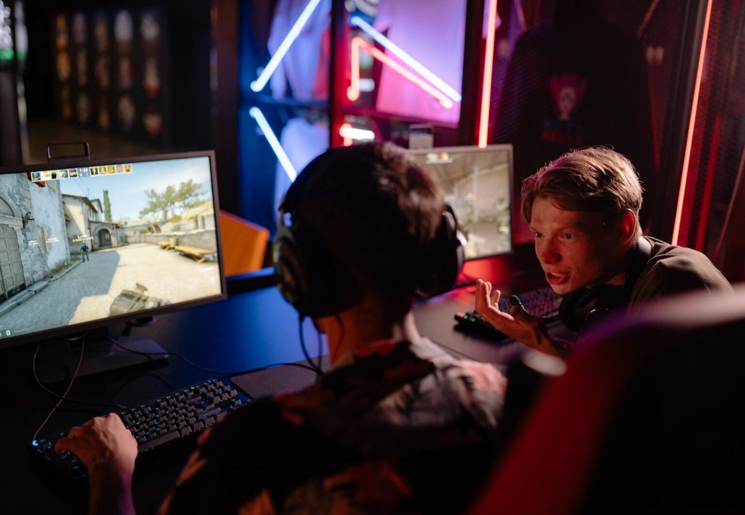 Two gamers engaged in a heated video game session surrounded by neon lights and computer screens.